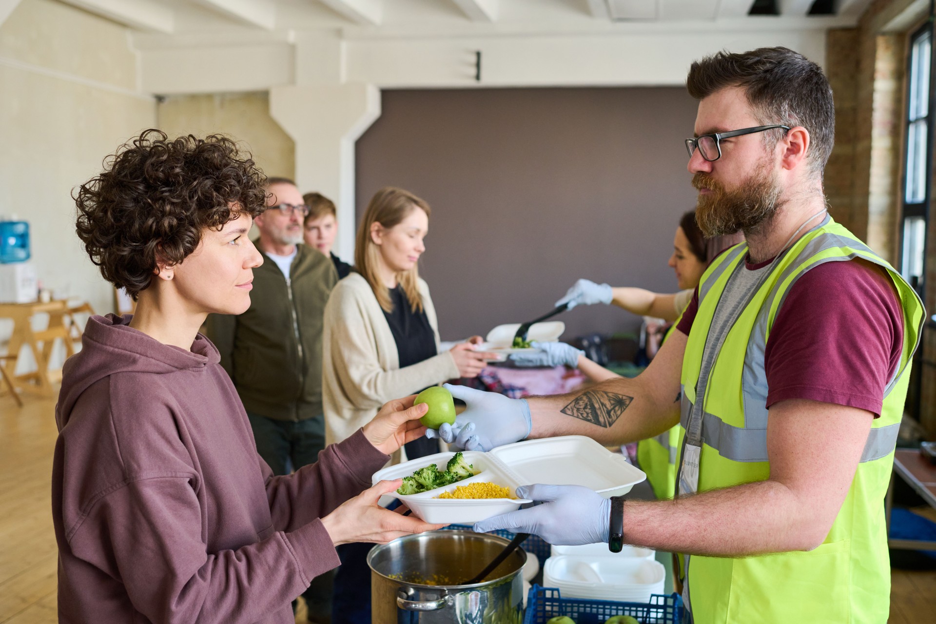 Young serious female migrant taking container with food and looking at volunteer