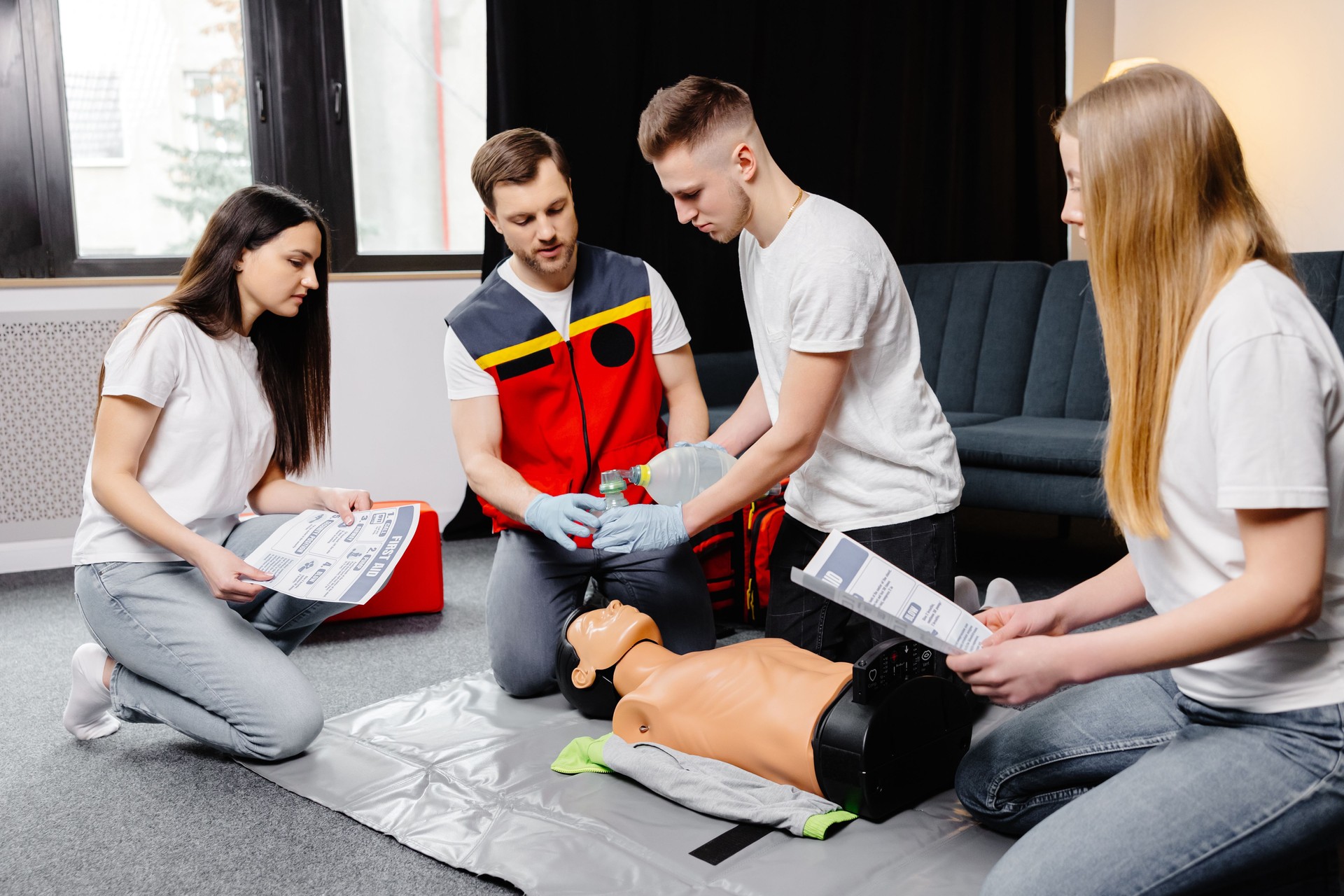 Young man instructor helping to make first aid heart compressions with dummy during the group training indoors